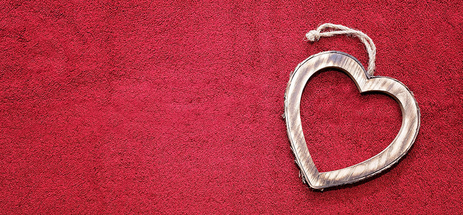 A wooden heart ornament lying on a red textured background.