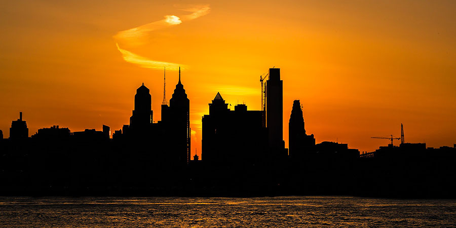 Philadelphia skyline along the Delaware River, at sunset with an orange sky
