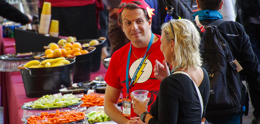 two WordCamp attendees chat by the snack table, which has trays of vegetables and fruit bins