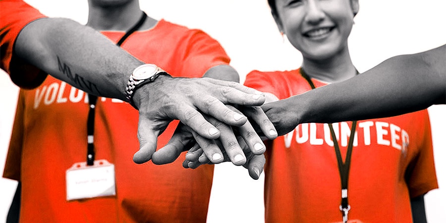 Four people in red shirts marked Volunteer joining hands